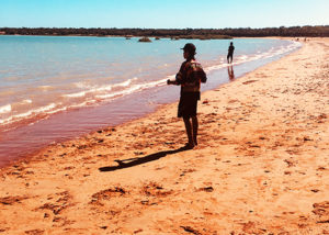 teenage male from youth justice program stands on the beach fishing in broome