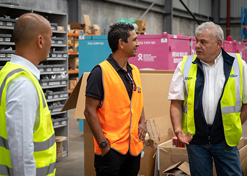 troy cook stands with 2 men from amcap in high vis vests in warehouse